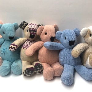 May include: Six knitted teddy bears in various colors, including pink, blue, and beige. The bears are all sitting down and have black eyes and noses.