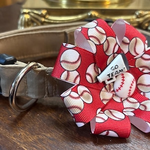 May include: Tan dog collar with a black buckle and a silver metal ring. A red bow with baseballs and a small white megaphone that says "GO TEAM!" is attached to the collar. A small baseball is also attached.