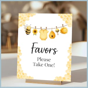 May include: A rectangular sign with a gold stand features a watercolor design with a bee theme. The sign reads "Favors, Please Take One!" and includes illustrations of a bee, sunflower, baby clothes, and a beehive.