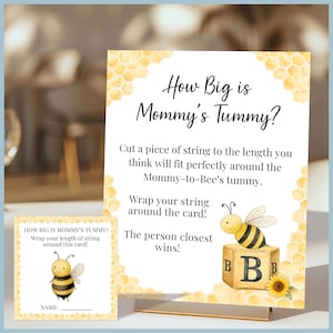 May include: A baby shower game with a bee theme. The main sign reads "How Big is Mommy's Tummy?" and includes instructions. A smaller card with a bee graphic and space for a name is also present. The design features yellow and white colours.