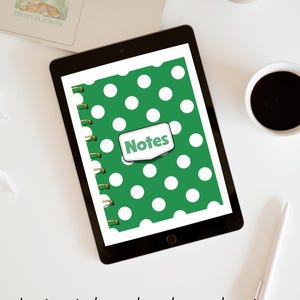 May include: A digital tablet displaying a green notebook cover with a white polka dot pattern and a central white label featuring the word Notes in green text. The notebook has a gold spiral binding on the left side and is shown on a white desk.