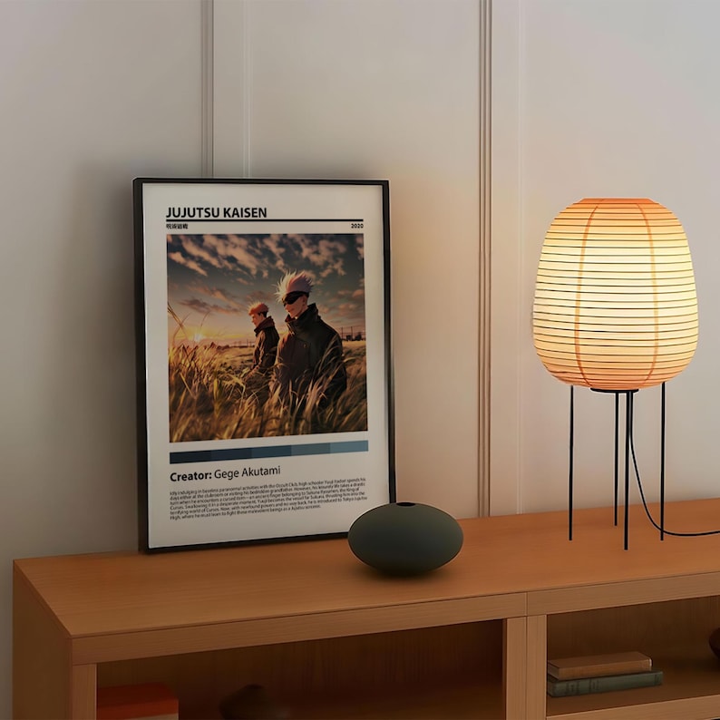May include: A black framed poster with the title "JUJUTSU KAISEN" and a picture of two anime characters standing in a field. The poster also includes the text "Creator: Gege Akutami". A black and white vase and a brown and white lamp are on a wooden shelf.