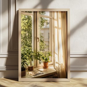 Può includere: Uno specchio da parete rettangolare con cornice in legno chiaro che riflette una finestra. Il riflesso mostra una finestra con tende trasparenti, piante verdi in vaso su un davanzale e la luce del sole che proietta ombre all'interno.