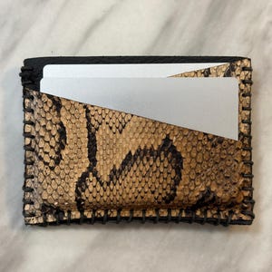 Pu&ograve; includere: Un piccolo porta carte in pelle nera con un motivo a pelle di serpente. Il porta carte ha un bordo cucito e uno slot per carte argentato.