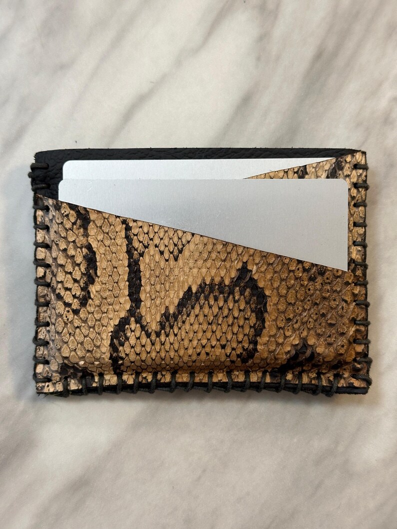 Pu&ograve; includere: Un piccolo porta carte in pelle nera con un motivo a pelle di serpente. Il porta carte ha un bordo cucito e uno slot per carte argentato.