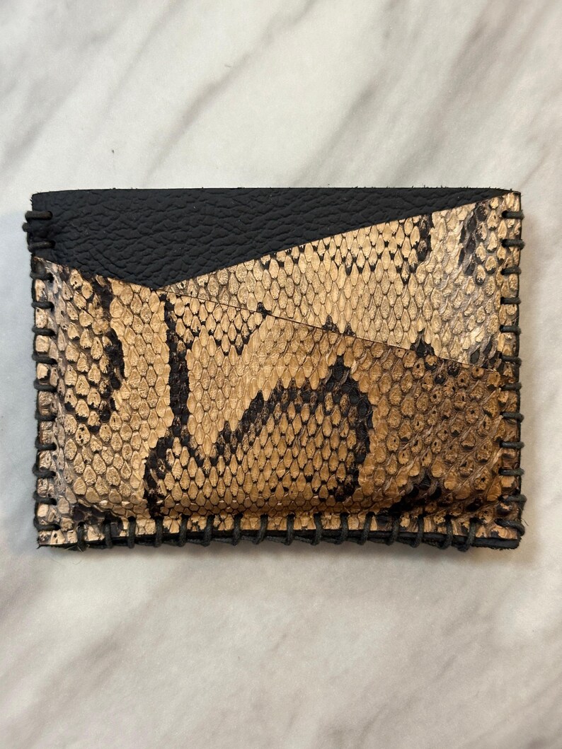 Pu&ograve; includere: Un piccolo portafoglio in pelle di serpente nero e oro con un bordo cucito.