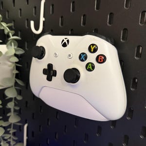 May include: A white Xbox controller with black buttons and a black faceplate. The controller has a black and white Xbox logo on the top and the letters X, Y, A, and B on the front.