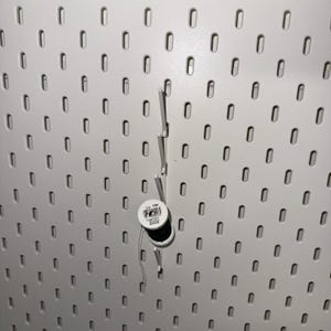 May include: A white pegboard with a black spool of thread hanging from a white peg. The spool has a label that reads "Col. 794".