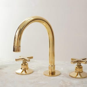 May include: A gold-toned bathroom faucet with a curved spout and two cross-shaped handles.
