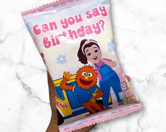 May include: A pink and white party favor bag with the text "Can you say Birthday?" and cartoon characters. The bag features a pink scalloped top and a marble background.