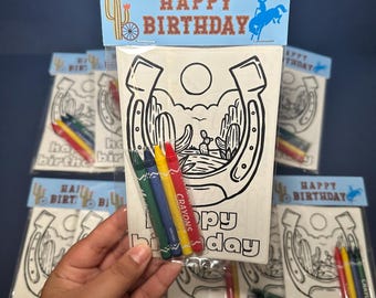 May include: Packaged birthday coloring sets featuring a horseshoe and desert scene design. Each set includes a coloring page and a pack of crayons. The top of the package reads "HAPPY BIRTHDAY" with a cowboy and cactus illustration.