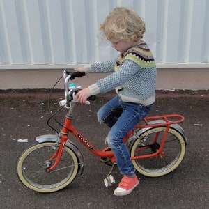 Puede incluir: Una persona joven montando una bicicleta roja con neum&aacute;ticos blancos y un asiento negro. La bicicleta tiene una campana plateada y un manillar cromado. La persona lleva un su&eacute;ter azul y blanco y pantalones vaqueros azules.