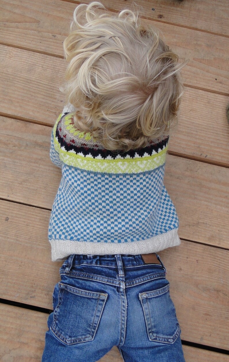 Puede incluir: Un ni&ntilde;o lleva un su&eacute;ter azul y blanco con un borde verde, amarillo y negro. El ni&ntilde;o tambi&eacute;n lleva pantalones vaqueros azules.