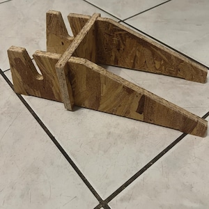 Op de afbeelding: Twee houten plankdragers gemaakt van oriented strand board (OSB). Elke beugel heeft een driehoekige vorm met een gekerfde bovenkant om een plank te ondersteunen. De beugels zijn lichtbruin van kleur met zichtbare houtnerf.