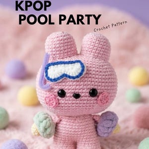 May include: A pink crocheted amigurumi figure with two ears, black eyes, and pink cheeks. It wears a white and blue snorkel mask and holds small textured spheres in each hand. Text reads Ebook KPOP POOL PARTY Crochet Pattern.