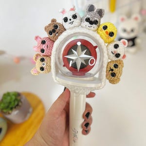 May include: A white light stick with a clear plastic sphere containing a red star. The sphere is surrounded by eight crocheted animal figures, including a bunny, a pig, a chick, and a bear.