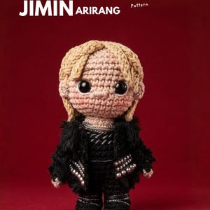 Pode incluir: Boneca de crochê de uma pessoa com cabelo loiro, vestindo uma roupa preta com tachas prateadas e uma jaqueta de pele sintética. A boneca tem olhos grandes e pretos e está em um fundo vermelho. O texto "EBOOK JIMIN ARIRANG Crochet Pattern" é visível.