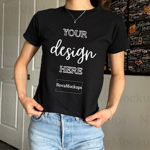 May include: A black t-shirt with short sleeves and a crew neck. The shirt has the text "YOUR design HERE" and "NovaMockups" printed on the front in white.
