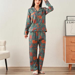 May include: A two-piece pajama set in a teal floral print. The long-sleeved top has a button-down front and a notched collar. The matching pants are loose-fitting. The floral pattern includes orange and red roses.