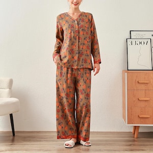 Op de afbeelding: Een tweedelige pyjamaset met een blouse met knopen en een bijpassende broek. De set is bruin van kleur met een bloemenpatroon in oranje en rode tinten. De pyjama heeft lange mouwen en een relaxte pasvorm, ideaal om in te slapen.