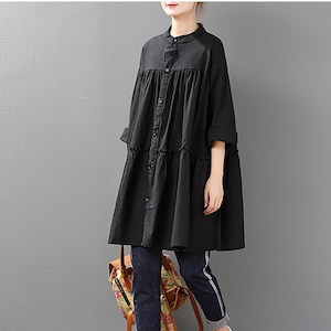 Puede incluir: Vestido túnica negro de manga larga con botones y bajo con volantes. El vestido se combina con vaqueros oscuros, zapatillas blancas y una mochila estampada. El vestido tiene cuello mandarín y mangas tres cuartos.