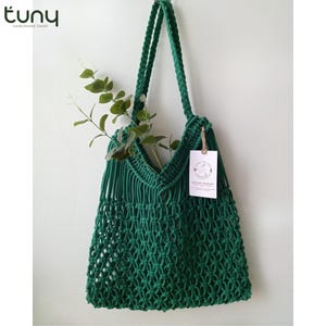 May include: A green crocheted tote bag with a fringe detail and a small tag that says "Tiny Handmade Shop".