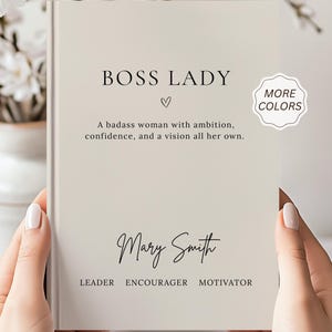 Może przedstawiać: Beżowa książka w twardej oprawie z czarnym napisem BOSS LADY, ikoną serca oraz frazą A badass woman with ambition, confidence, and a vision all her own. Poniżej wydrukowano imię Mary Smith, a następnie słowa LEADER ENCOURAGER MOTIVATOR.