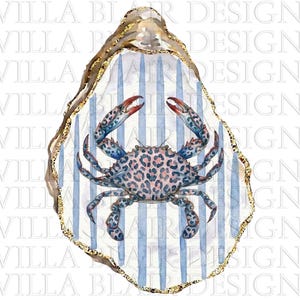 May include: A decorative oyster shell featuring a central crab illustration with a pink and blue leopard print pattern. The shell background displays vertical light blue stripes, and the outer edge is finished with a textured gold metallic trim.