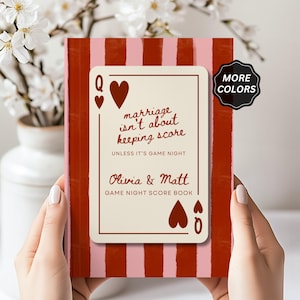 May include: A game night score book with a red and pink striped cover. The front features a cream-colored playing card graphic with the text: marriage isn't about keeping score UNLESS IT'S GAME NIGHT, Olivia & Matt, GAME NIGHT SCORE BOOK.