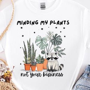 A cute raccoon with eyes closed in from of plants that reads I Mind my plants not your business. Sarcastic Raccoon Png | Funny Plant Lover png | Sarcastic Gardening Humor png | Trendy Plant Lover DOWNLOAD ONLY