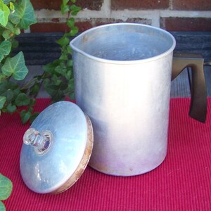 May include: A silver aluminum coffee pot with a black handle and a separate lid. The pot has a rounded body and a slightly flared top.