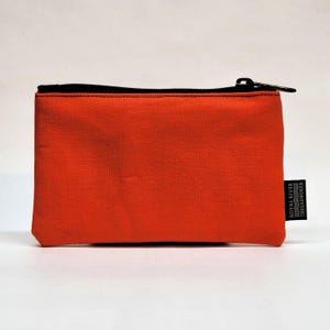 May include: A bright orange zippered pouch with a black zipper and a black label that reads "Royal River Threadworks".