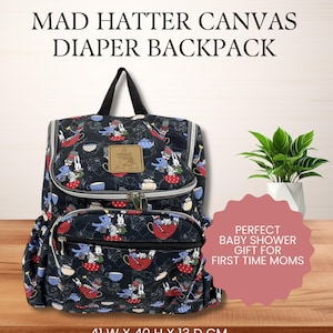 May include: Black canvas diaper backpack with a Mad Hatter design. The backpack features a whimsical pattern of teacups, rabbits, and hats. It measures 41 cm wide, 40 cm high, and 13 cm deep. The text on the bag reads "MAD HATTER CANVAS DIAPER BACKPACK".