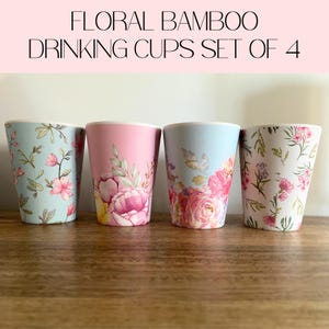 May include: A set of four floral bamboo drinking cups. Each cup has a different pastel colour and floral design. The colours include light blue, pink, and white. The text "FLORAL BAMBOO DRINKING CUPS SET OF 4" is at the top.