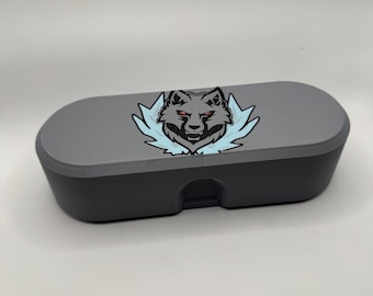 May include: A gray, oblong, 3D-printed storage case with a flat top and rounded ends. Centered on the lid is a graphic illustration of a wolf head with red eyes, surrounded by light blue, jagged, flame-like shapes on a white background.