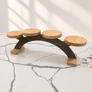 May include: A wooden display stand featuring a dark-stained arched base with two small rectangular feet and four light-colored circular platforms of varying heights arranged in a stepped, horizontal sequence for showcasing small items.