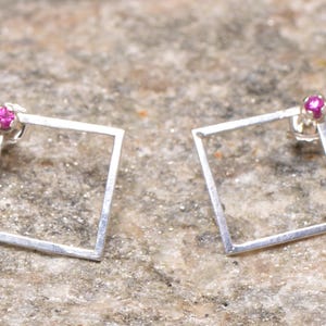 May include: A pair of silver square earrings with a small pink gemstone in the center of each square.
