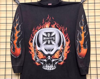 May include: A black long-sleeve shirt featuring a large graphic of a skull surrounded by orange and red flames. The skull has a Misfits logo inside an iron cross on its forehead. Both sleeves feature orange and red flame graphics along the arms.