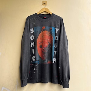 Op de afbeelding: Een antracietgrijs shirt met lange mouwen en een grafische print van een getextureerd oranje wezen op een blauwe achtergrond. De tekst SONIC YOUTH staat verticaal aan de zijkanten van de afbeelding, met het woord DIRTY in blauw onder het wezen.