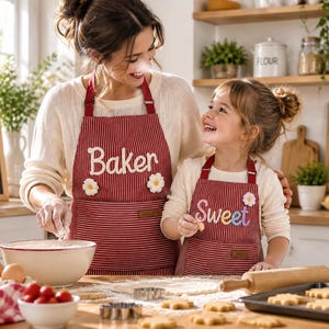 Può includere: Grembiuli coordinati a righe rosse e bianche con decorazioni a margherita bianca e scritte. Il grembiule da adulto riporta la parola Baker, quello da bambino la parola Sweet. Entrambi hanno una tasca frontale e lacci rossi regolabili.