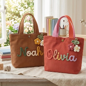 May include: Two corduroy tote bags, one brown and one terracotta, each featuring a snap closure and two handles. The brown bag displays the name Noah in green and yellow yarn, while the terracotta bag displays Olivia in multicolored yarn.