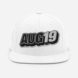 Pode incluir: Um boné de beisebol branco com o texto AUG19 bordado numa fonte preta, negrito e tridimensional nos painéis frontais. O boné tem uma copa estruturada, uma aba reta e um design limpo com um gráfico central em destaque e bem visível.