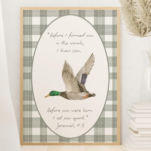 May include: A framed print with a green and white plaid background. The center features a white oval with a watercolor illustration of a duck in flight. The text reads "Before I formed you in the womb, I knew you. Before you were born I set you apart." Jeremiah 1:5