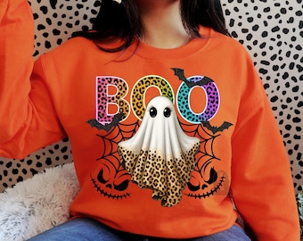May include: Orange sweatshirt with a Halloween-themed design. The word "BOO" is in colorful leopard print letters. A cartoon ghost with a leopard print bottom is in the center, surrounded by bats and spiderwebs.