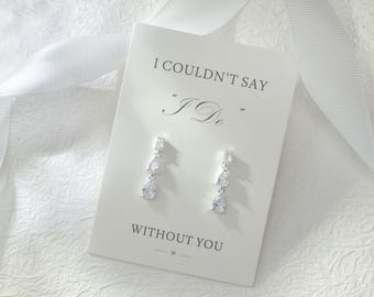 May include: A pair of silver-toned drop earrings with clear teardrop-shaped stones attached to a white display card. The card features the black printed text I COULDN'T SAY "I DO" WITHOUT YOU. A white ribbon is positioned behind the display card.