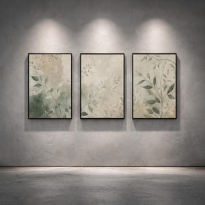 Può includere: Tre stampe artistiche botaniche incorniciate. Ogni stampa presenta una palette di colori tenui di verdi, beige e bianchi, con delicati disegni di foglie e rami. Le cornici nere sono montate su un muro grigio, creando un set coesivo.