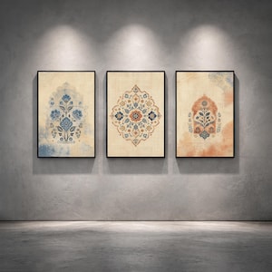 Könnte beinhalten: Drei gerahmte Wandkunstwerke mit aufwendigen floralen Designs. Das Kunstwerk zeigt einen beigefarbenen Hintergrund mit blauen, orangefarbenen und braunen Blumenmustern. Jedes Stück ist in einem schwarzen Rahmen gerahmt und an einer grauen Wand ausgestellt.