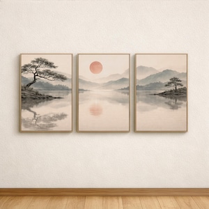 以下が含まれることがあります： 3枚組の額入り風景画プリント。各プリントは、山、木、夕日を配した穏やかな湖の風景を描いています。アートワークはベージュ、グレー、ピーチの落ち着いた色調で、穏やかな美しさを生み出しています。