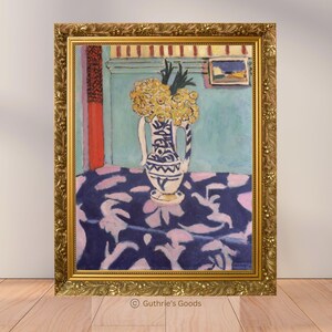 May include: A framed painting featuring a still life with a vase of yellow flowers on a table with a blue and pink patterned tablecloth. The vase is white with blue designs. The frame is gold.