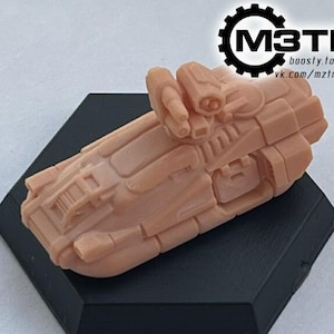 May include: A light brown, futuristic spacecraft model with detailed paneling and cylindrical components, resting on a black hexagonal base. The model has a textured surface and is likely a 3D-printed item. The image includes the text "M3TM" and website information.